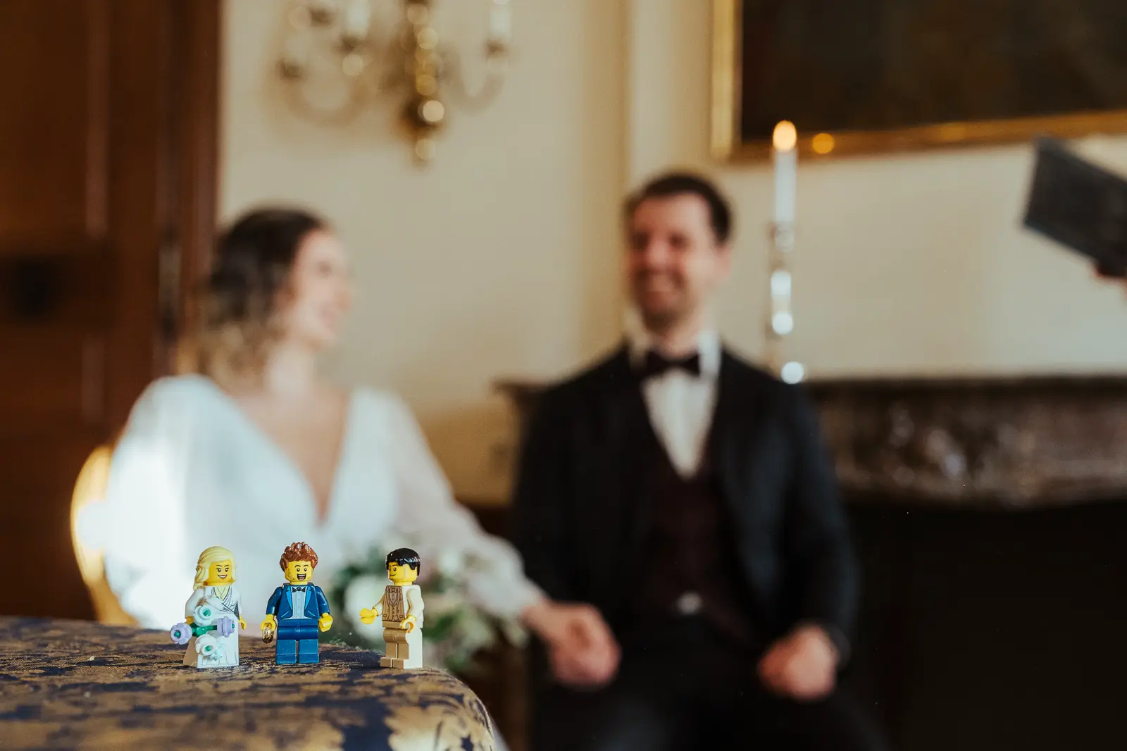 Lego-Brautpaar von Jasmin & Tobi im Vordergrund, unscharf im Hintergrund die echte Trauung auf Schloss Beuggen.
